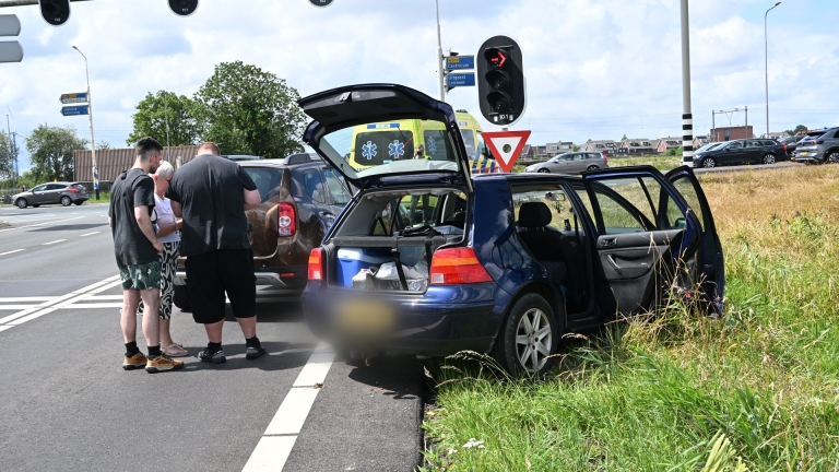 Hulpverleners verzorgen een slachtoffer naast een auto op een afgezet wegvak met pionnen en hulpdiensten op de achtergrond