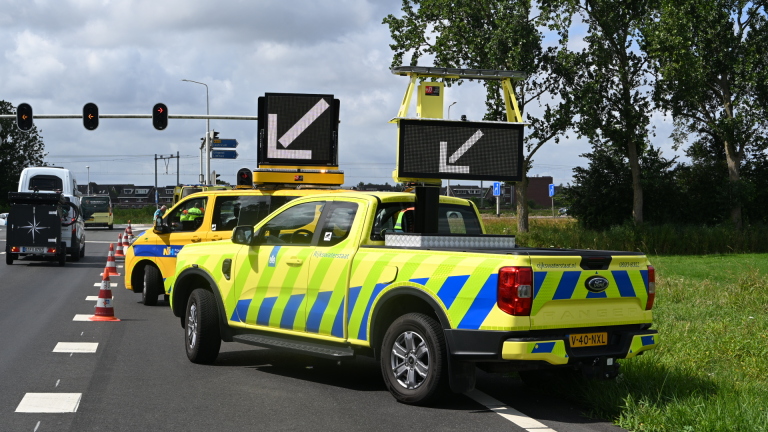 Hulpverleners verzorgen een slachtoffer naast een auto op een afgezet wegvak met pionnen en hulpdiensten op de achtergrond