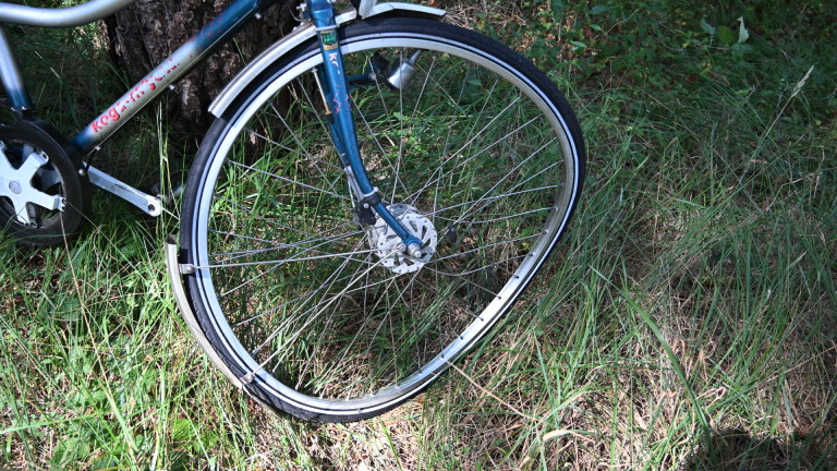 Gele ambulance op een bospad, met fietsers en omstanders eromheen tussen hoge bomen