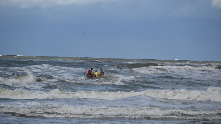 Reddingsbrigade in oranje rubberboot vaart over ruwe zee, met windturbines op de horizon