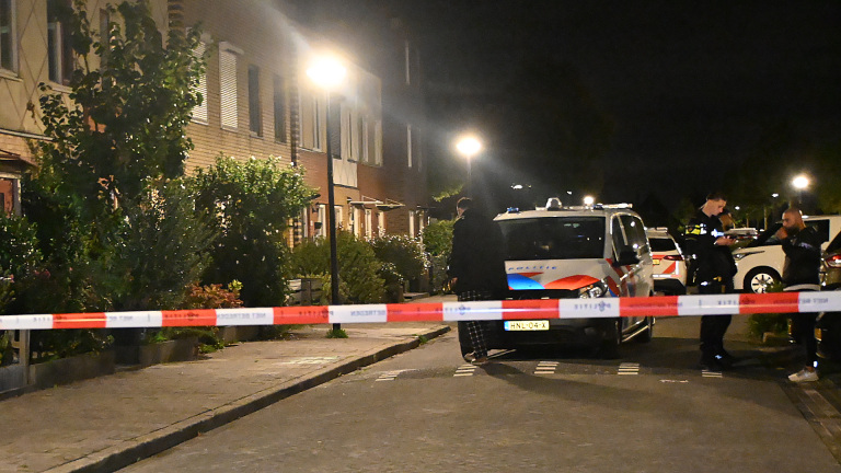 Groep politieagenten in uniform staat ’s avonds bij een bakstenen gebouw en overlegt met elkaar