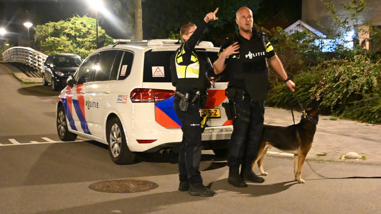Groep politieagenten in uniform staat ’s avonds bij een bakstenen gebouw en overlegt met elkaar