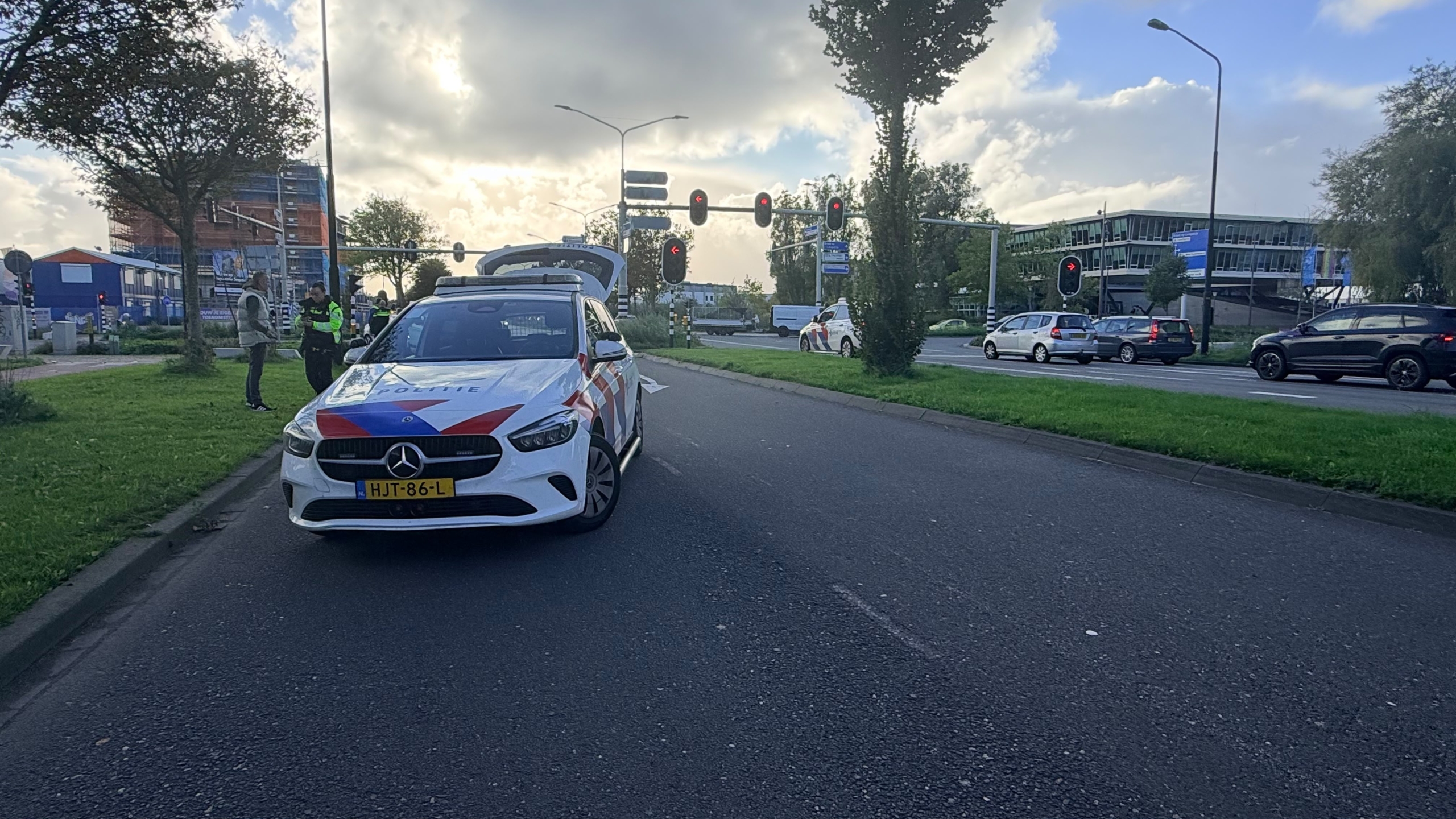 Witte bestelbus met ingedeukte motorkap na aanrijding op kruispunt, met politieauto en pionnen op de weg